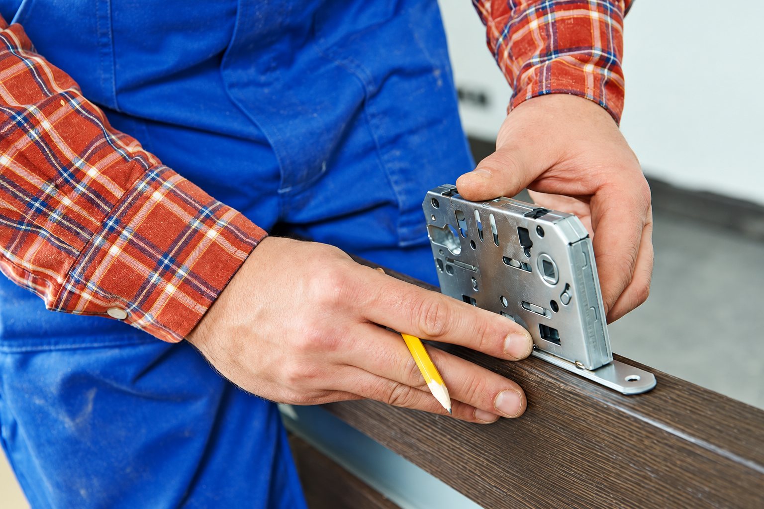 Artisan en salopette bleue positionnant une serrure encastrable sur une porte en bois