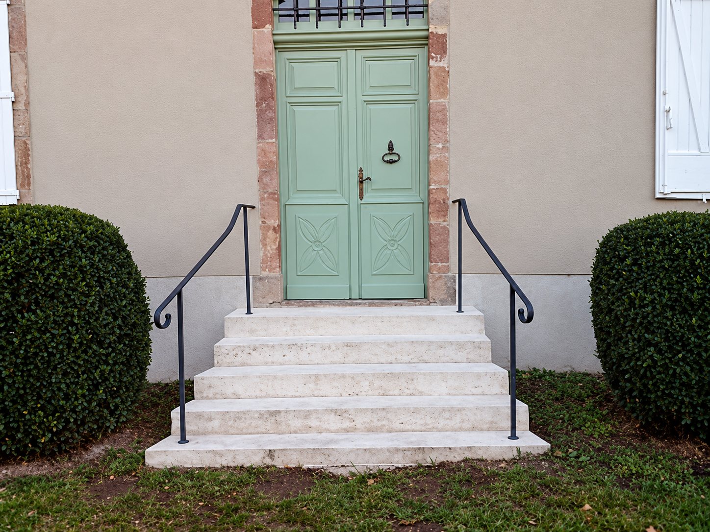 Escalier en pierre avec rampes en fer forgé devant une porte verte