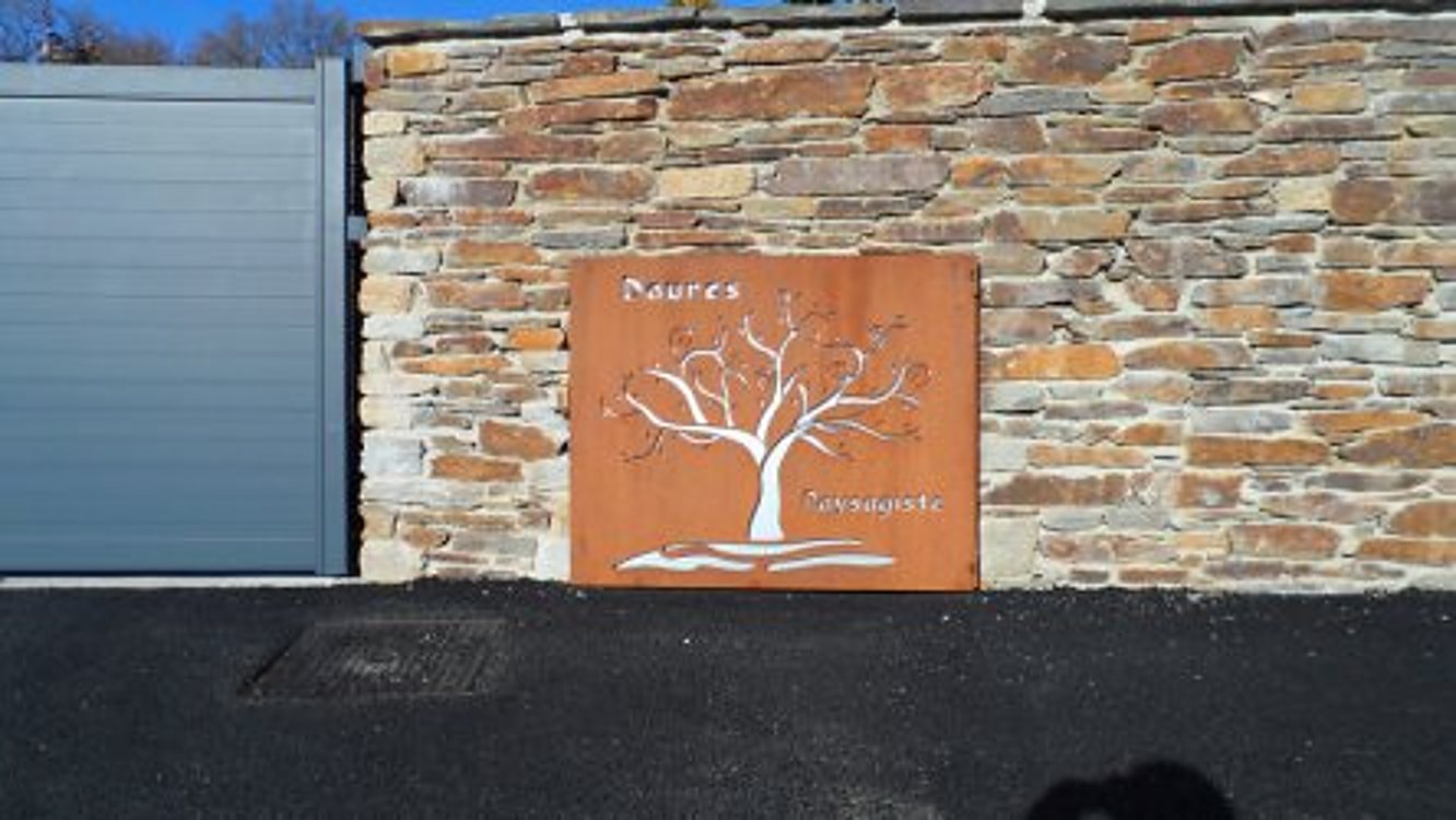 Panneau en acier corten découpé en forme d’arbre sur muret en pierre