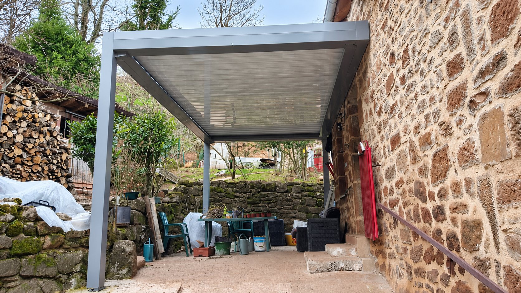 Pergola en aluminium gris adossée à un mur en pierre