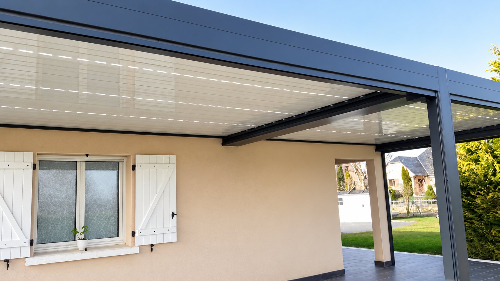Pergola bioclimatique grise à lames orientables installée contre une façade beige
