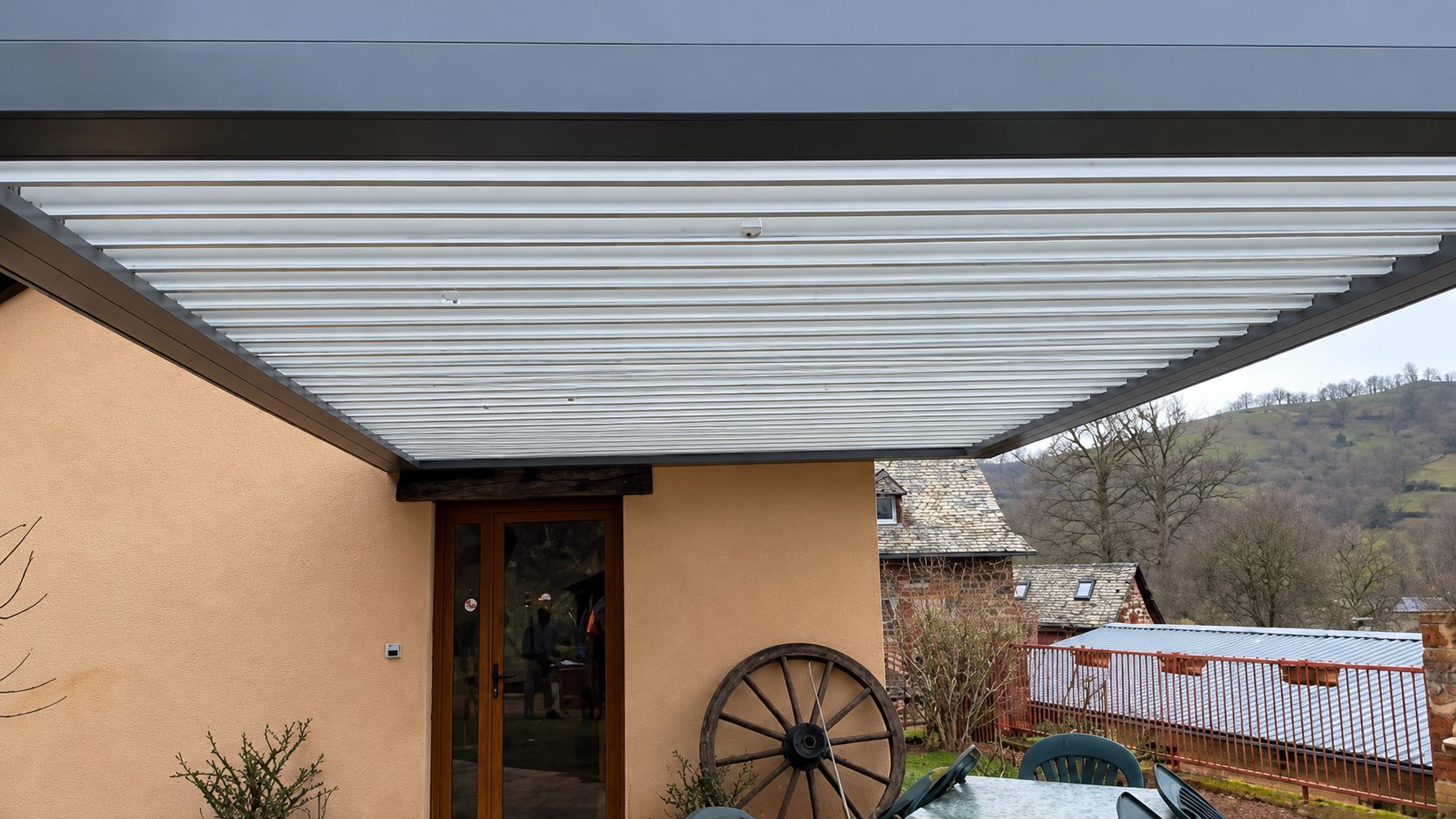 Pergola bioclimatique à lames blanches installée contre une maison en pierre à la campagne