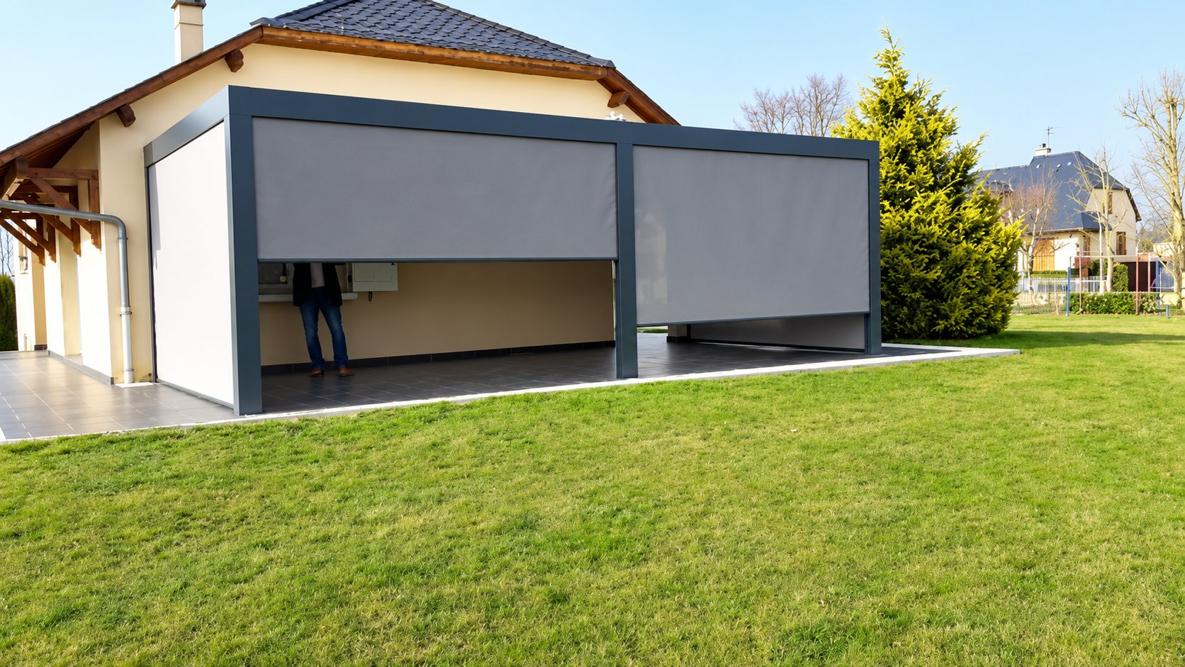 Pergola bioclimatique grise avec stores verticaux fermés devant une maison avec pelouse