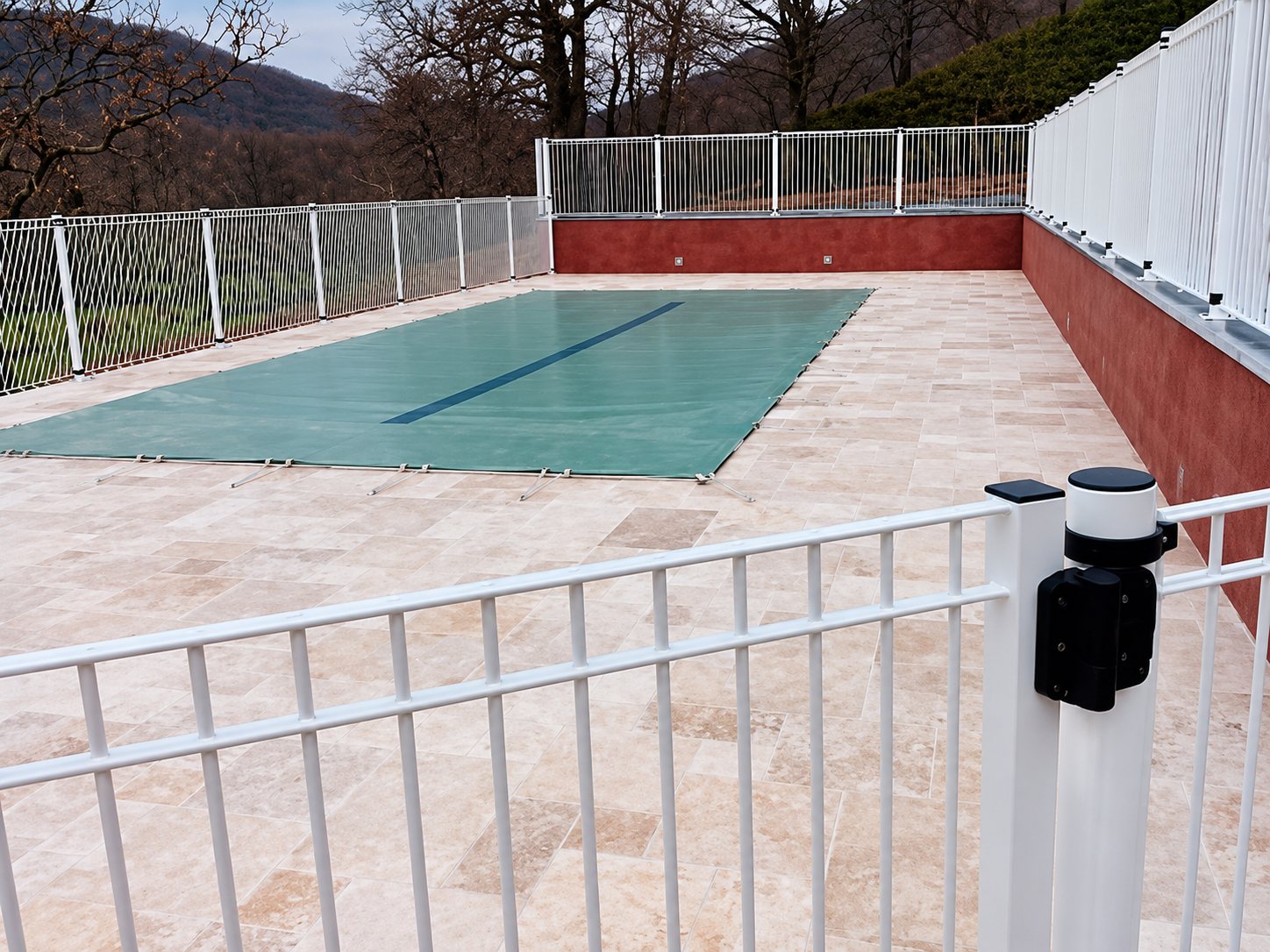 Piscine couverte d’une bâche verte avec barrière blanche et terrasse en pierre