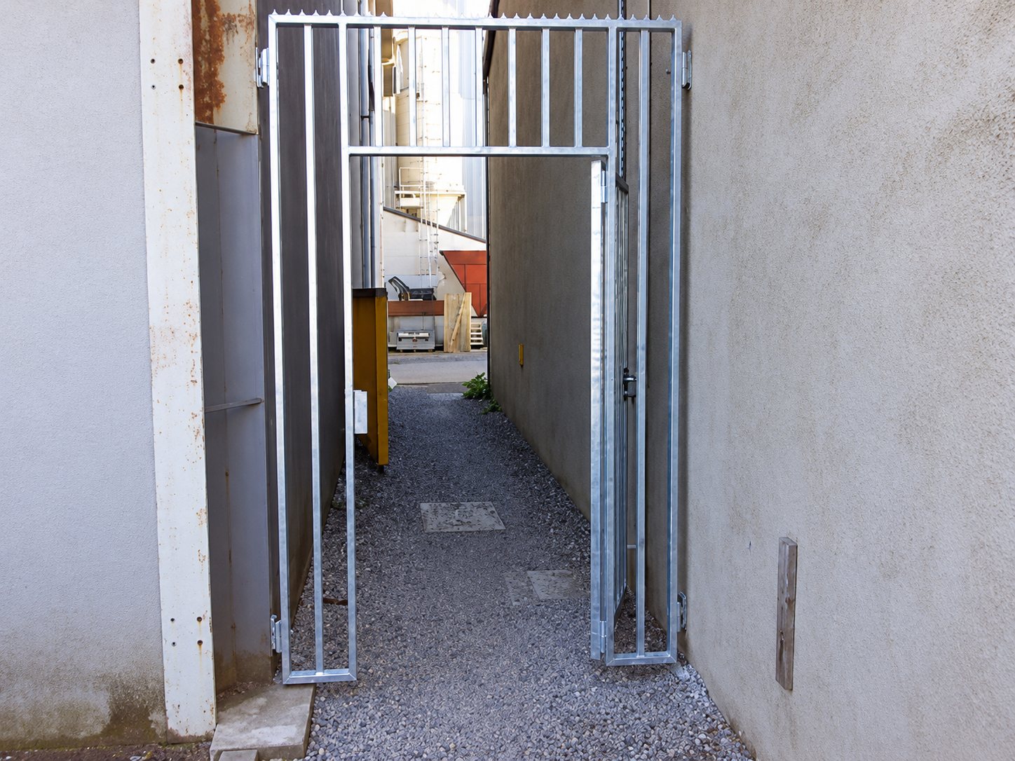 Portail métallique galvanisé à barreaux dans une ruelle étroite en gravier
