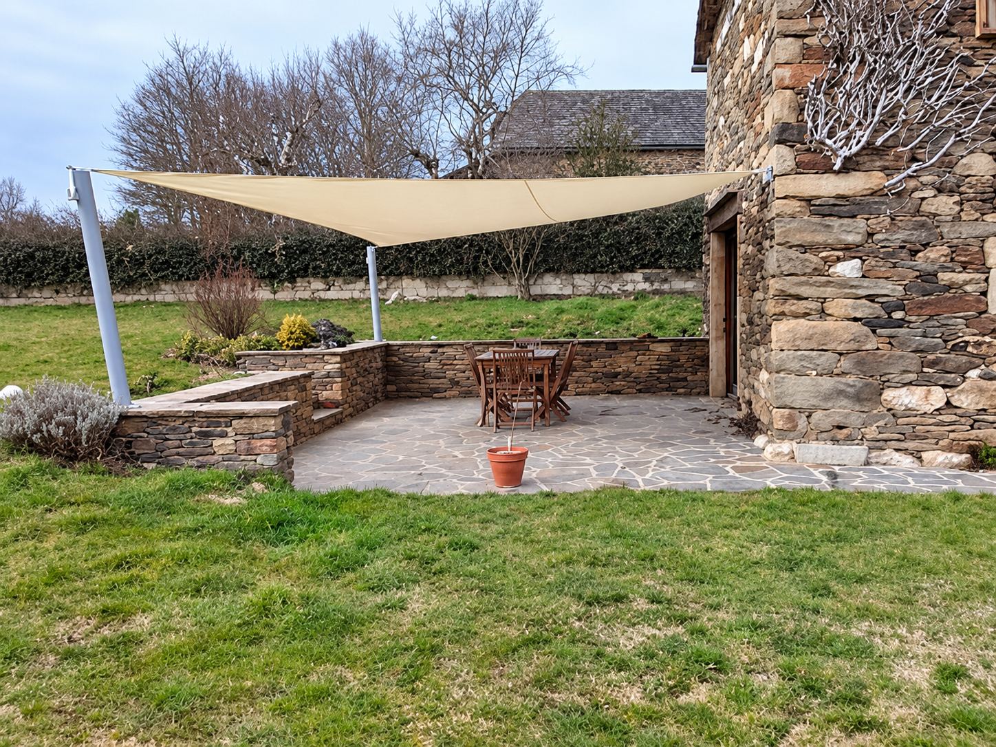 Terrasse en pierre avec voile d’ombrage tendue près d’une maison